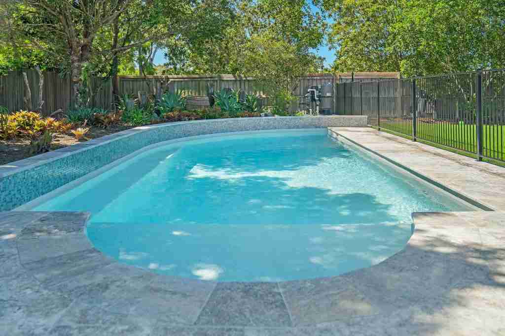 2023 SPASA award-winning freeform pool by Pool Fab, featuring a unique shape, curved wall with glass mosaic tiles, and sky-blue crystal water, set in a lush garden setting for outdoor entertaining - poolquotes.com.au