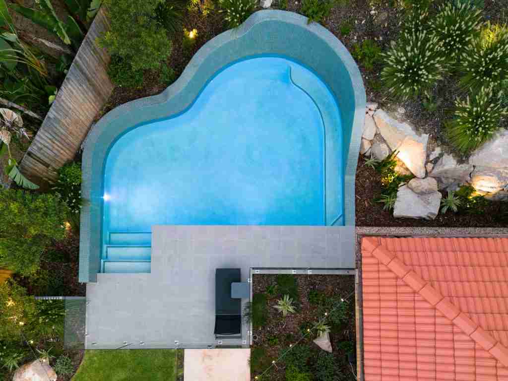 2023 QLD Best Freeform Pool award winner by Rogers Pools, a 7.0m x 5.0m unique curved pool with raised walls, blending seamlessly with natural rock surrounds, featured on poolquotes.com.au