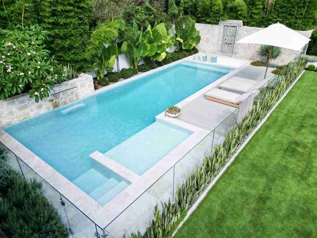 2023 NSW Best Concrete Pool award winner by Pinnacle Pools, featuring a 12m resort-like oasis with social zones, a large ledge for children, a tranquil water feature, and a sunken lounge under antique Indian doors, perfect for socialising and exercise, showcased on poolquotes.com.au