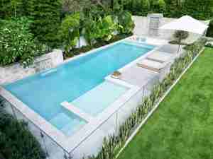 2023 NSW Best Concrete Pool award winner by Pinnacle Pools, featuring a 12m resort-like oasis with social zones, a large ledge for children, a tranquil water feature, and a sunken lounge under antique Indian doors, perfect for socialising and exercise, showcased on poolquotes.com.au